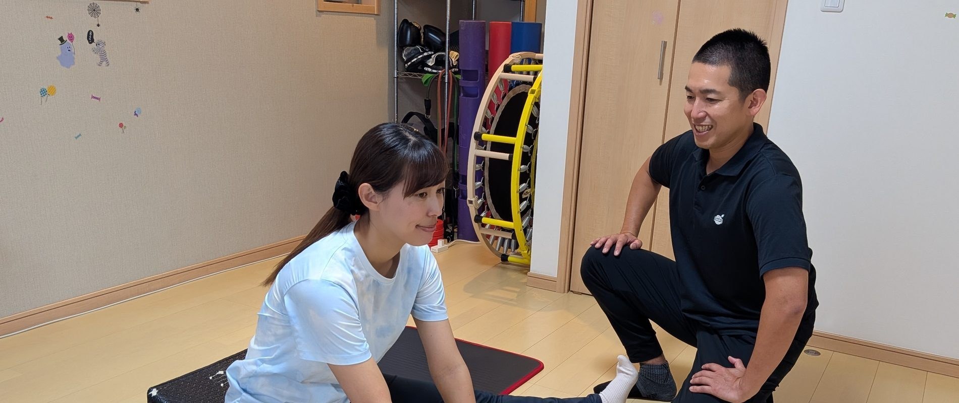 まちの隠れ家ジム宿河原で、トレーナーと一緒にストレッチをする様子